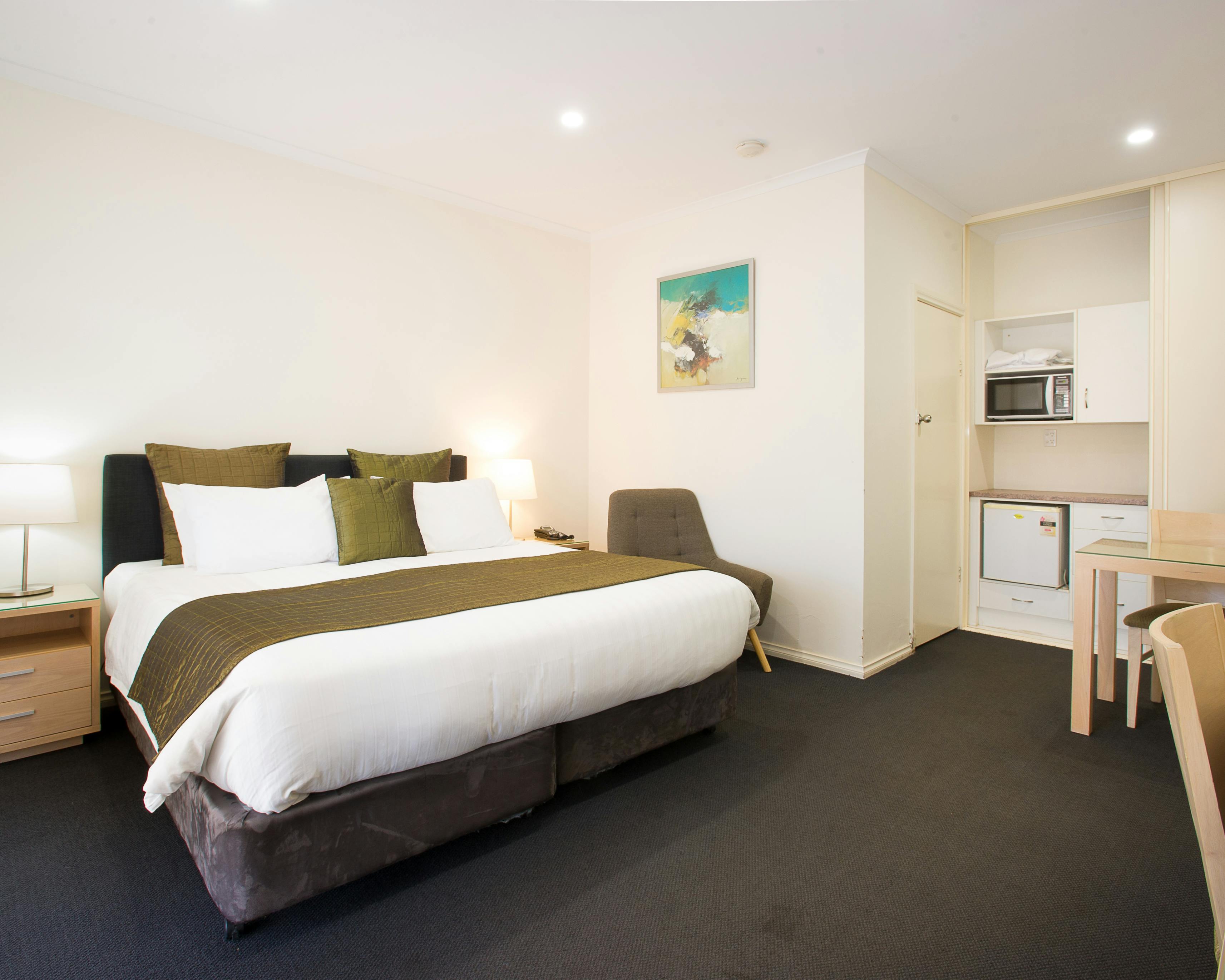 Modern motel room with king bed, kitchenette, & chair.