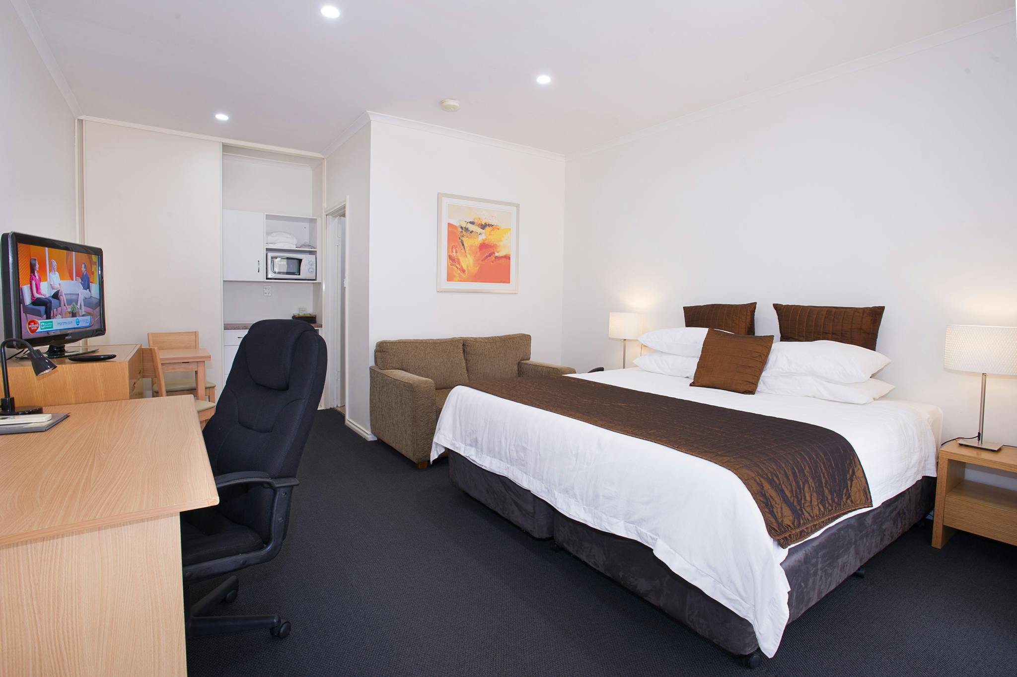 Clean motel room with bed, sofa, microwave, and TV.