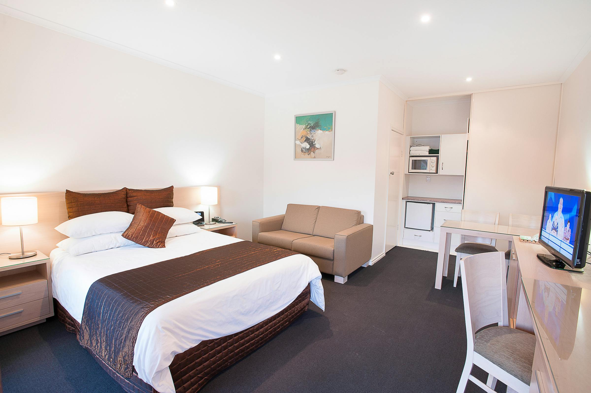 Clean, modern motel room with queen bed, sofa, microwave, and TV on a stand.