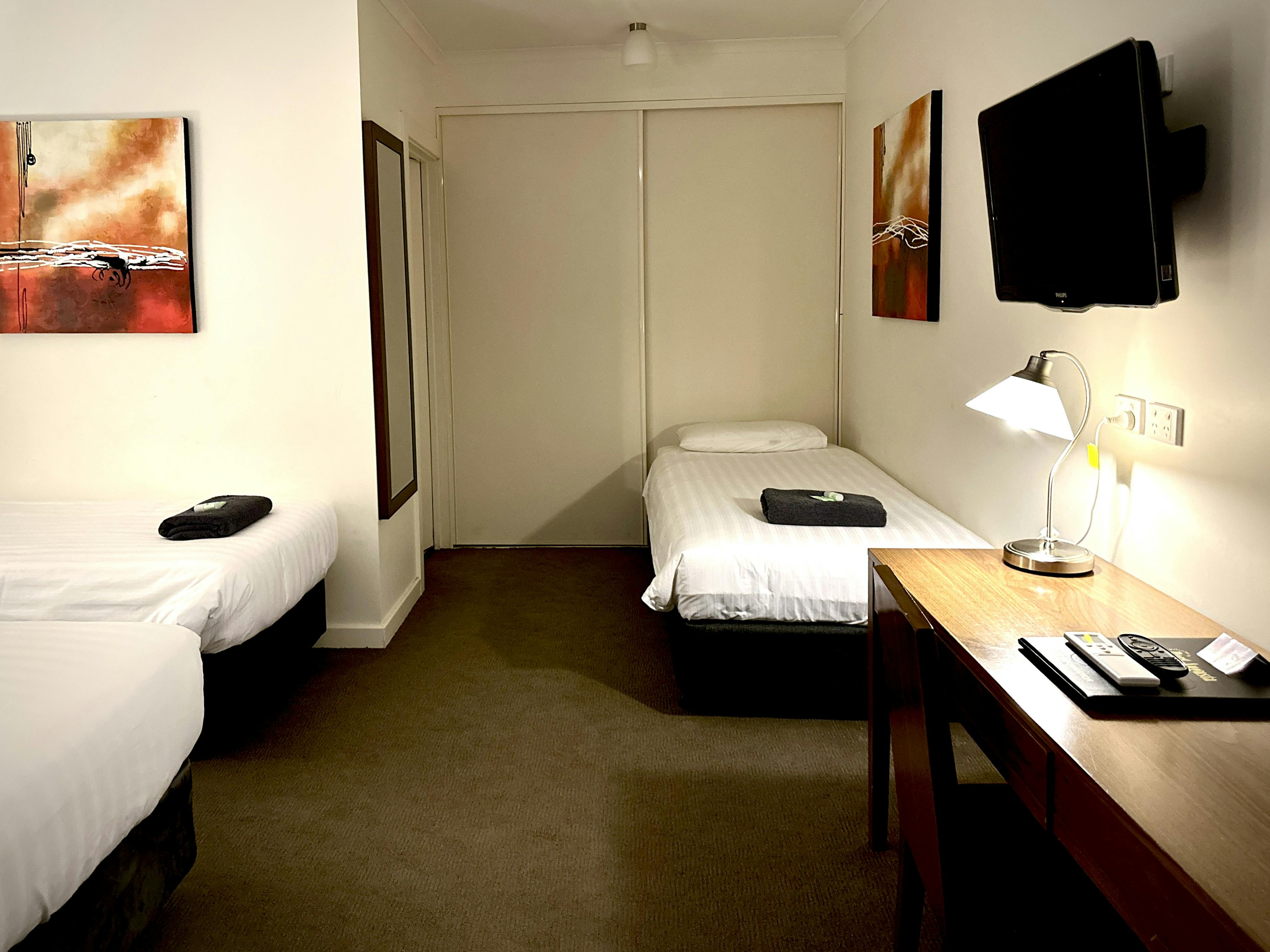 Simple, clean room. Two single beds. Neutral colors used. Functional furniture. Basic amenities.