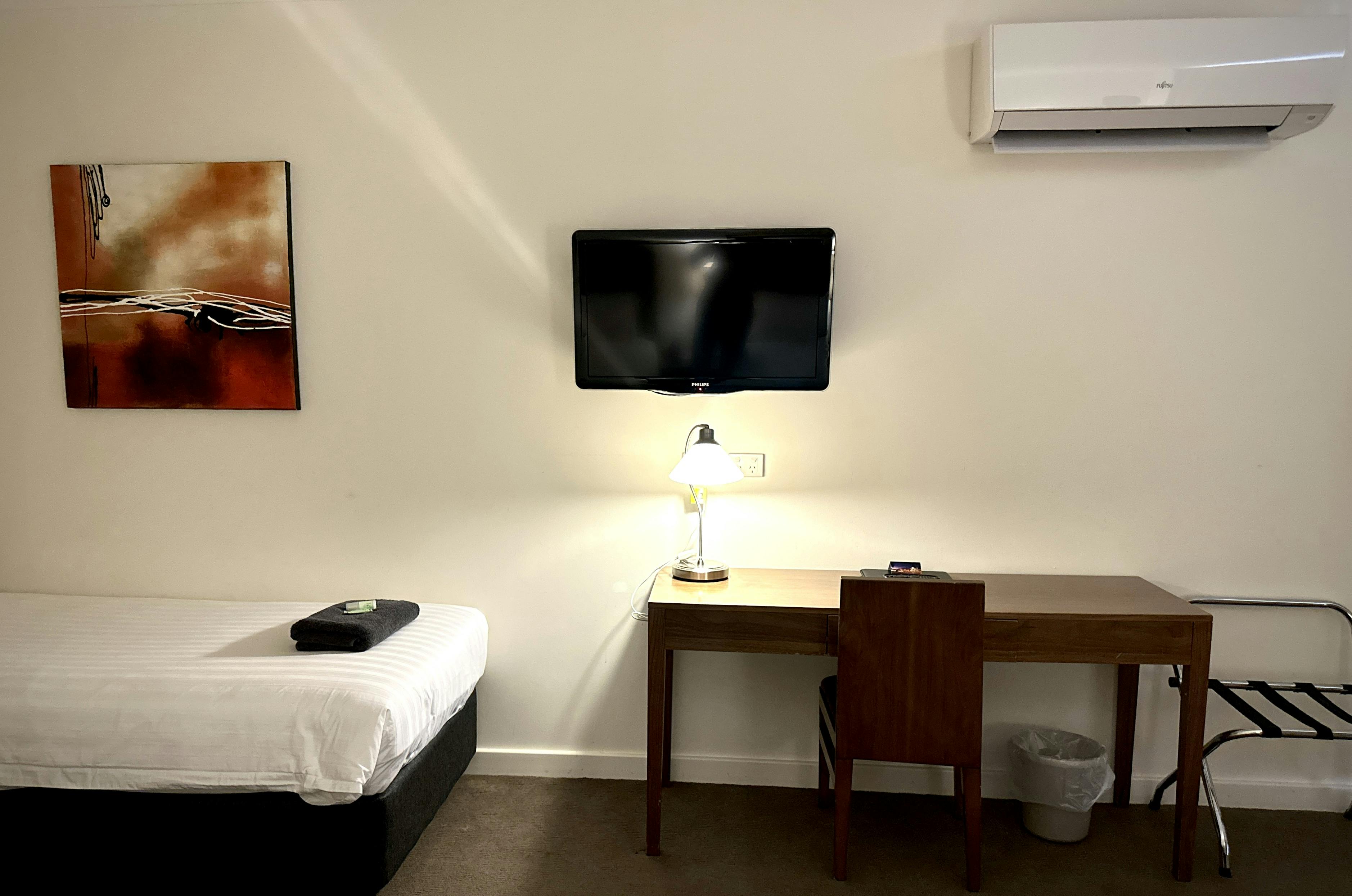 Room: 1 double, 2 singles, desk, TV, AC, art. Budget hotel room, sleeps 4, basic amenities.