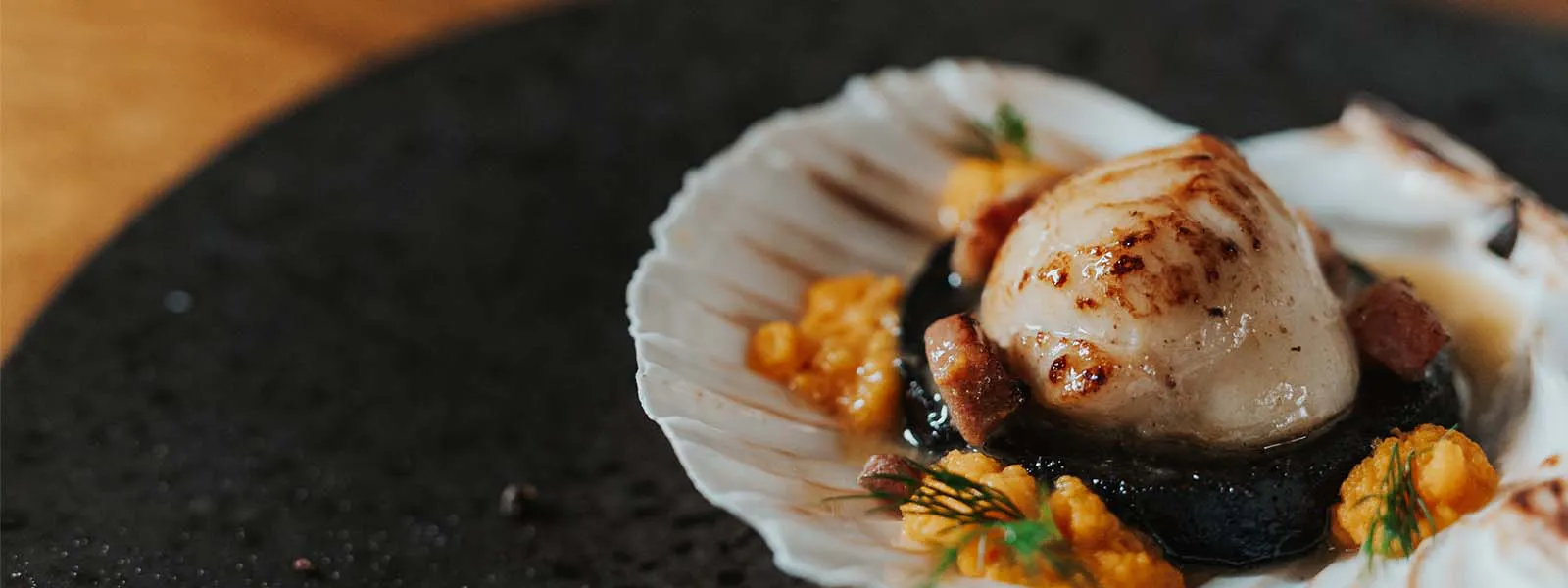 A beautifully presented scallop on a black plate, featured at the Boatshed Restaurant, Royal Hotel.