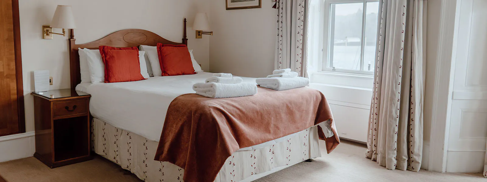 A cosy hotel room with a comfortable bed, a chair, and a window offering a scenic view.