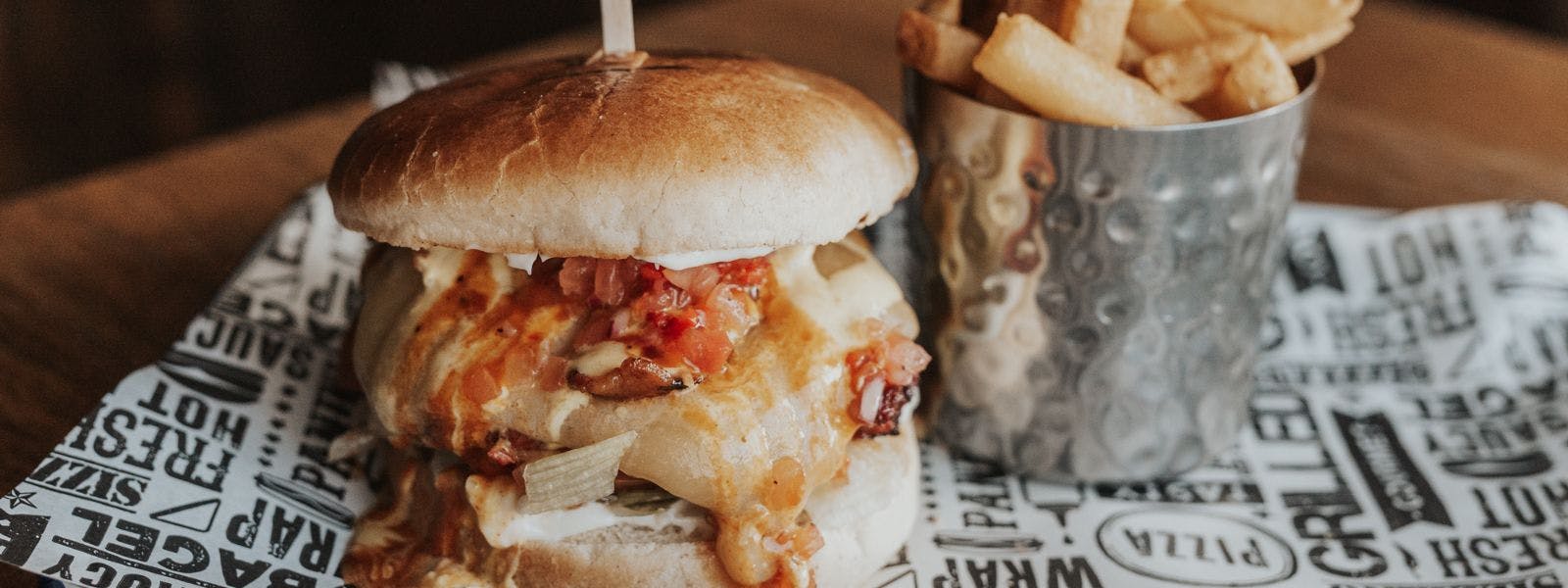 A large cheeseburger with crispy bacon and melted cheese on a paper plate, served with a side of chips.