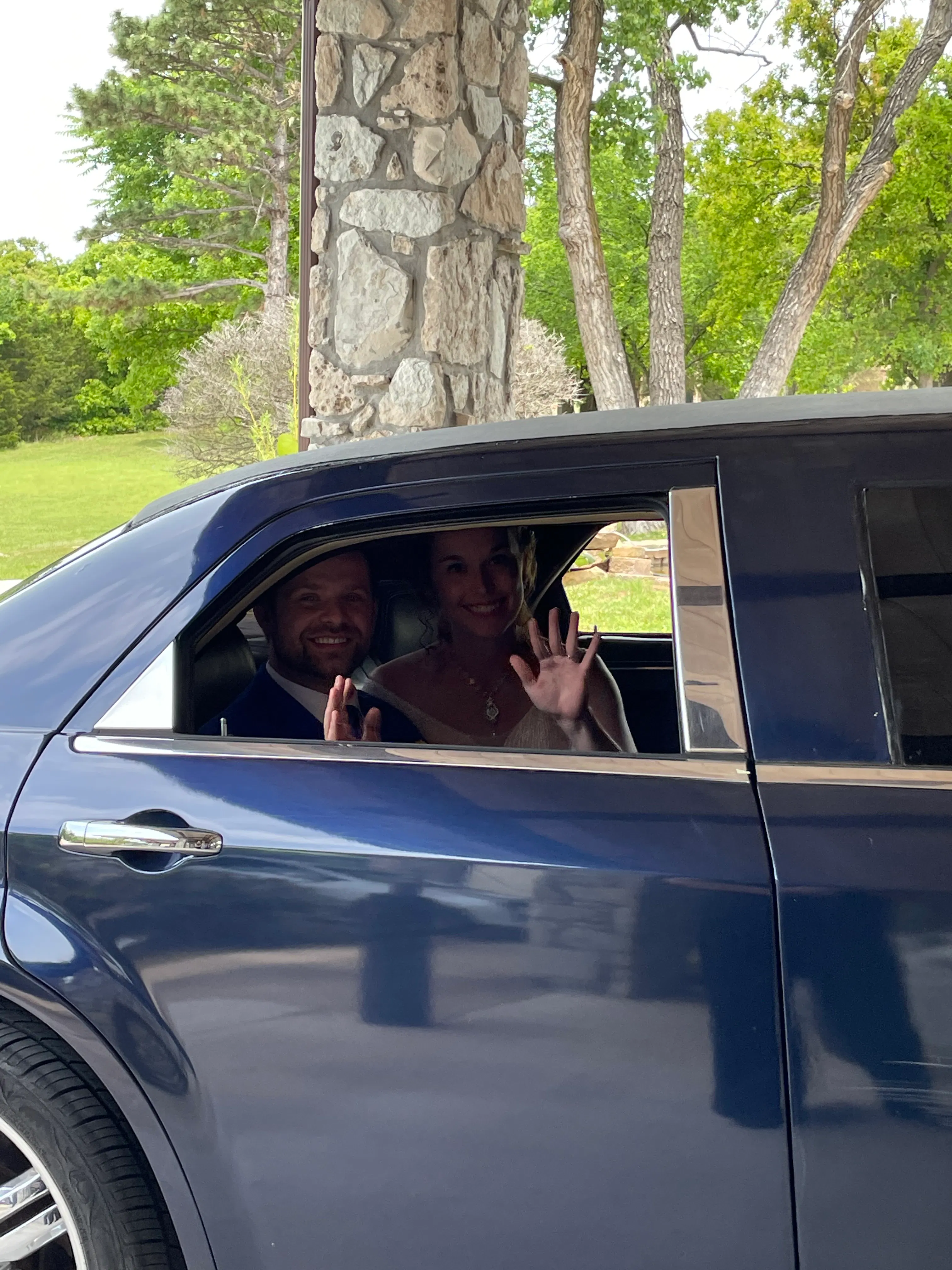 Bride and groom waving from a blue limousine