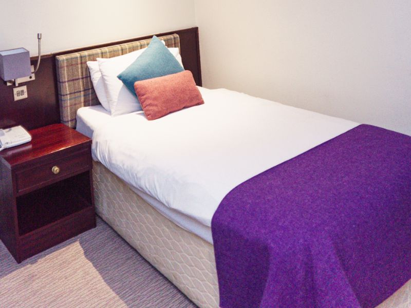 Single bed beds with colourful tweed blanket and cushions, check tweed headboard and neutral walls.