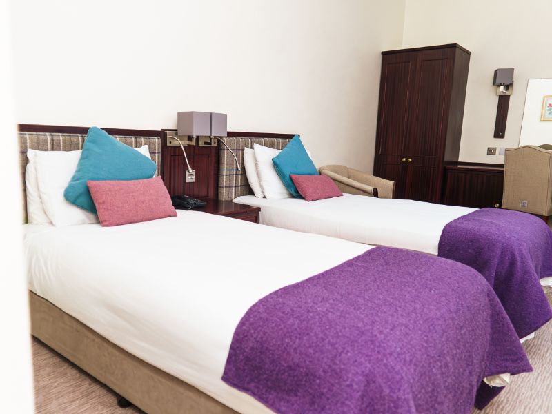 Twin beds with matching tweed blankets and cushions, check tweed headboards and neutral walls.