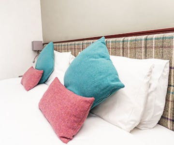 A cosy hotel bedroom with a comfortable bed with tweed cushions.