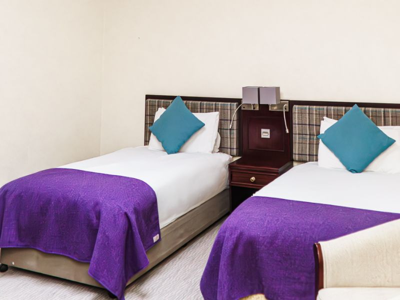 Twin beds with matching tweed blankets and cushions, check tweed headboards and neutral walls.