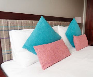 A cosy hotel bedroom with a comfortable bed with tweed cushions.