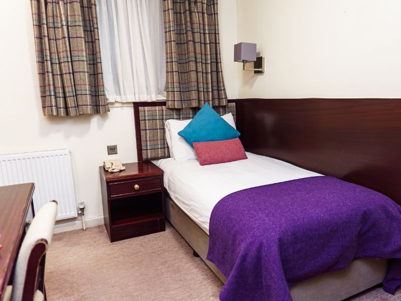 Single bed beds with colourful tweed blanket and cushions, check tweed headboard and curtains and neutral walls.