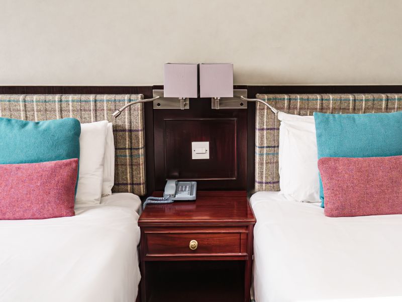 Two beds with blue and pink cushions and check tweed headboard.