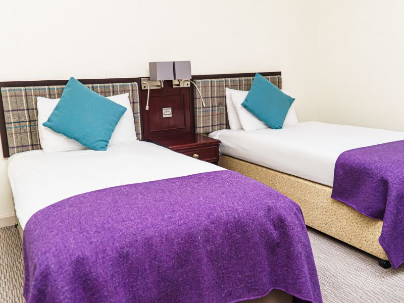 Twin beds with matching tweed blankets and cushions, check tweed headboards and neutral walls.