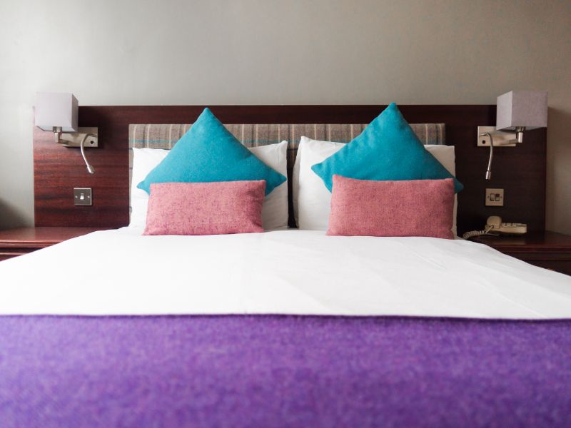 A cosy hotel bedroom with a comfortable bed with tweed cushions and throw, chair and a window with tweed curtains.