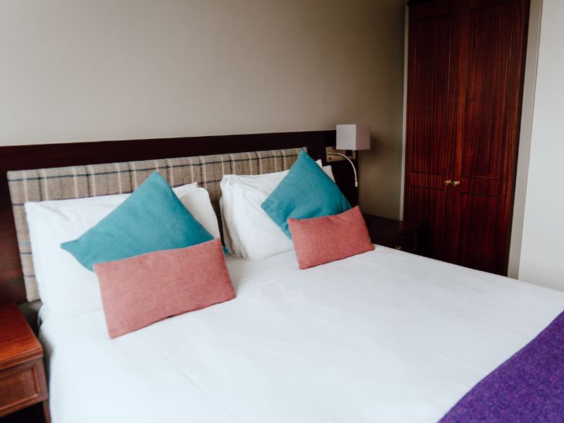 A cosy hotel bedroom with a comfortable bed with tweed cushions and throw.