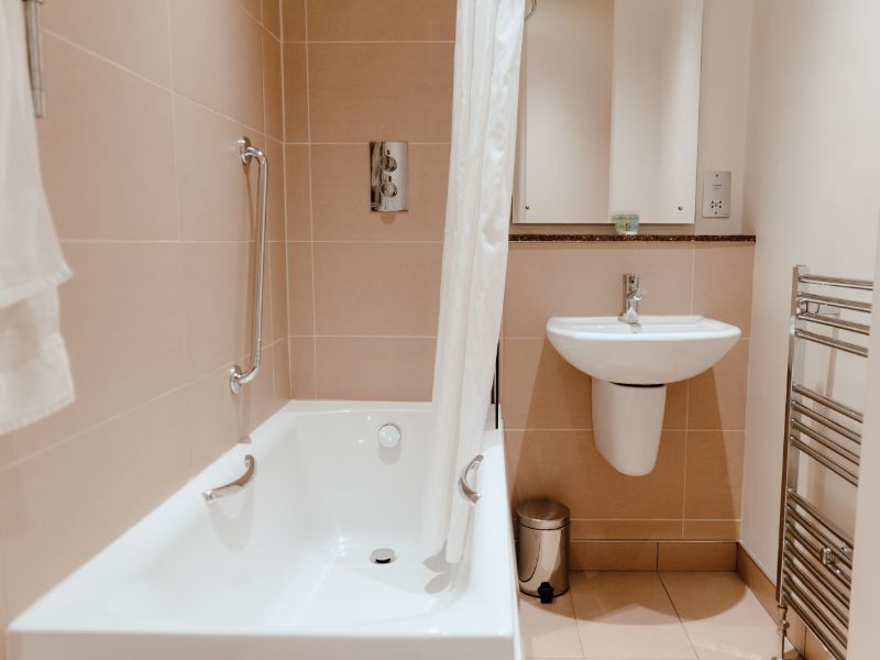 Modern bathroom with shower over bath and sink in neutral colours.