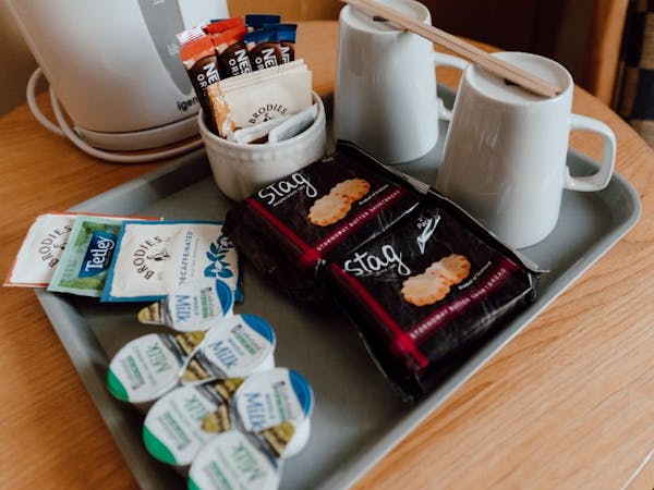 Tea and coffee station setup with kettle, cups, milk and biscuits on a tray placed on a wood table.