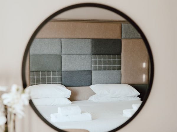 Round black mirror with reflection of white bed and check and plain tweed patchwork effect feature headboard.