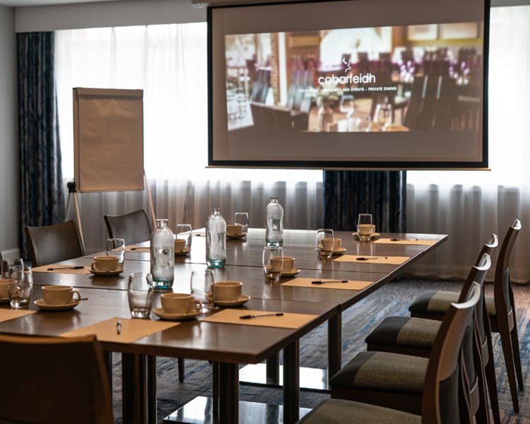 A conference room featuring a large projector screen at the front, ready for presentations and discussions.