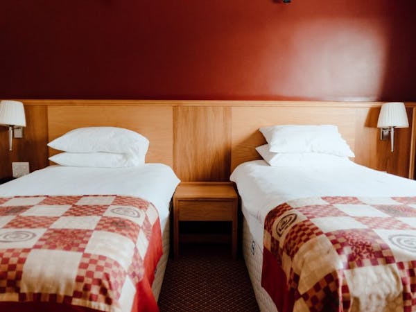 Twin room closeup with white bed linen, red check bed runner and deep red feature wall and wood panelling.