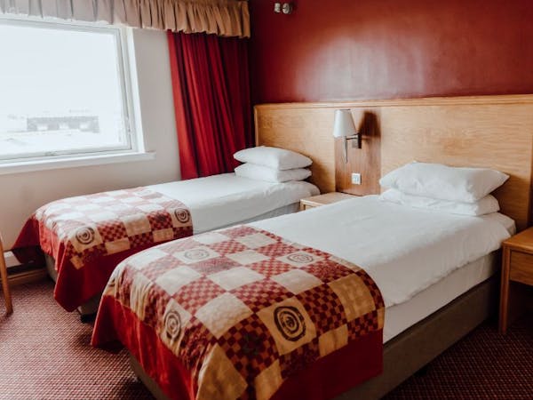Twin room with white bed linen, red check bed runner, deep red walls with large window with complimentary coloured curtains.
