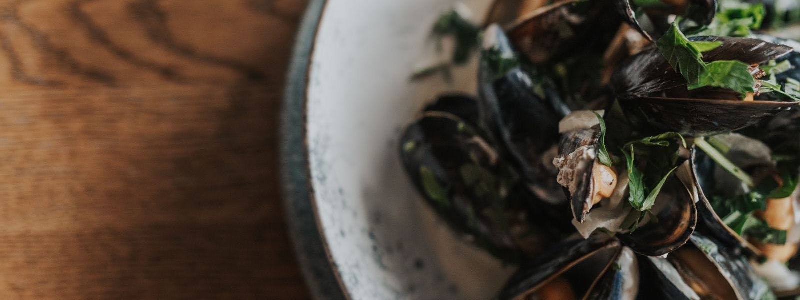 Close up of blue plate with mussels sitting on a wood table.