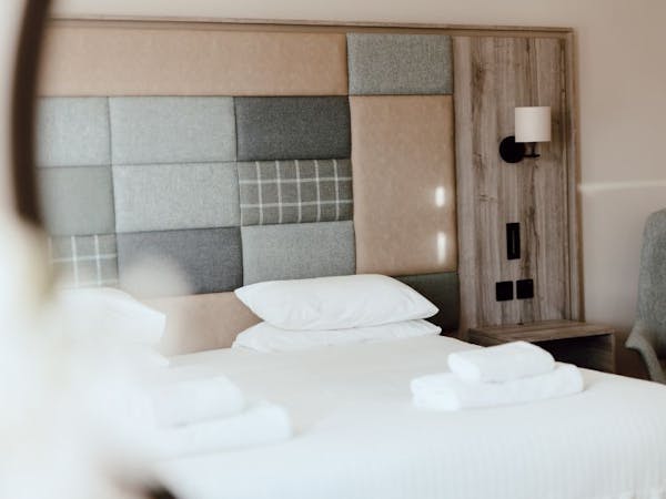 Double bedroom with white linen, check and plain tweed patchwork feature headboard, wall mounted lamps.