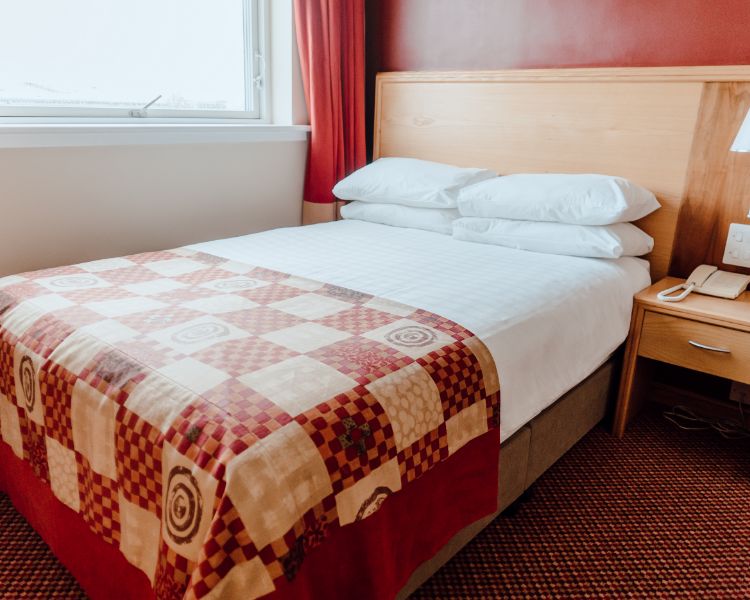Double room with white bed linen, red check bed runner, deep red walls. Large window with complimentary red curtains.