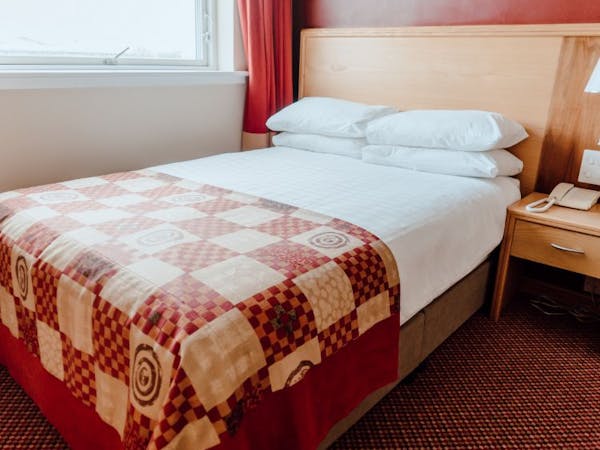 Double room with white bed linen, red check bed runner, deep red walls. Large window with complimentary red curtains.