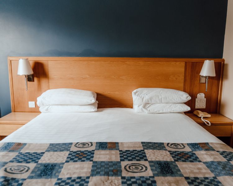 Double room with white bed linen, blue check bed runner, deep blue walls with wood panelling and wall mounted lamps.