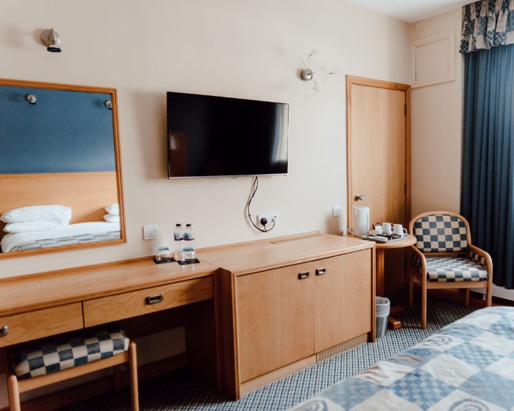 Bedroom setup with wood furniture and blue carpeting and furnishings, wall mounted TV and mirror and seating area to the left