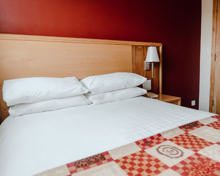 Double room closeup with white bed linen, red check bed runner, deep red walls.