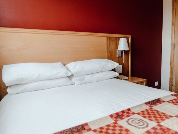 Double room closeup with white bed linen, red check bed runner, deep red walls.