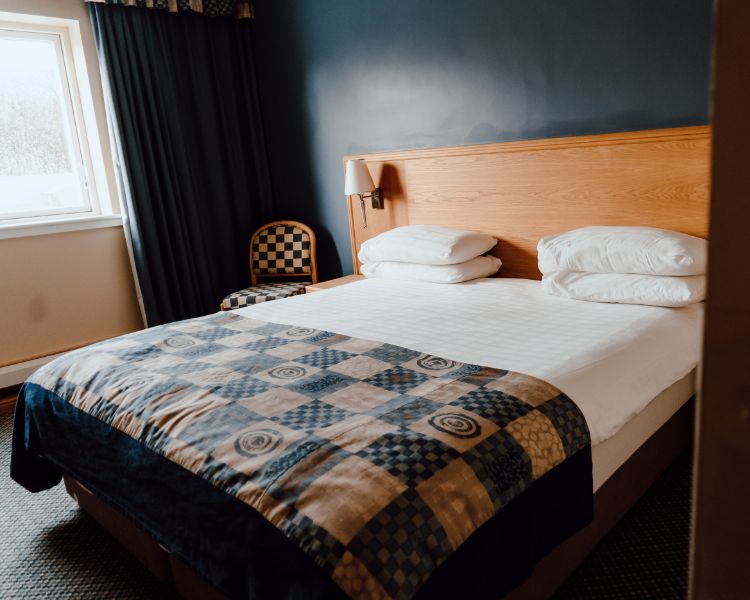 Double room with white bed linen, blue check bed runner, complimenting chairs and curtains. Deep blue feature wall.