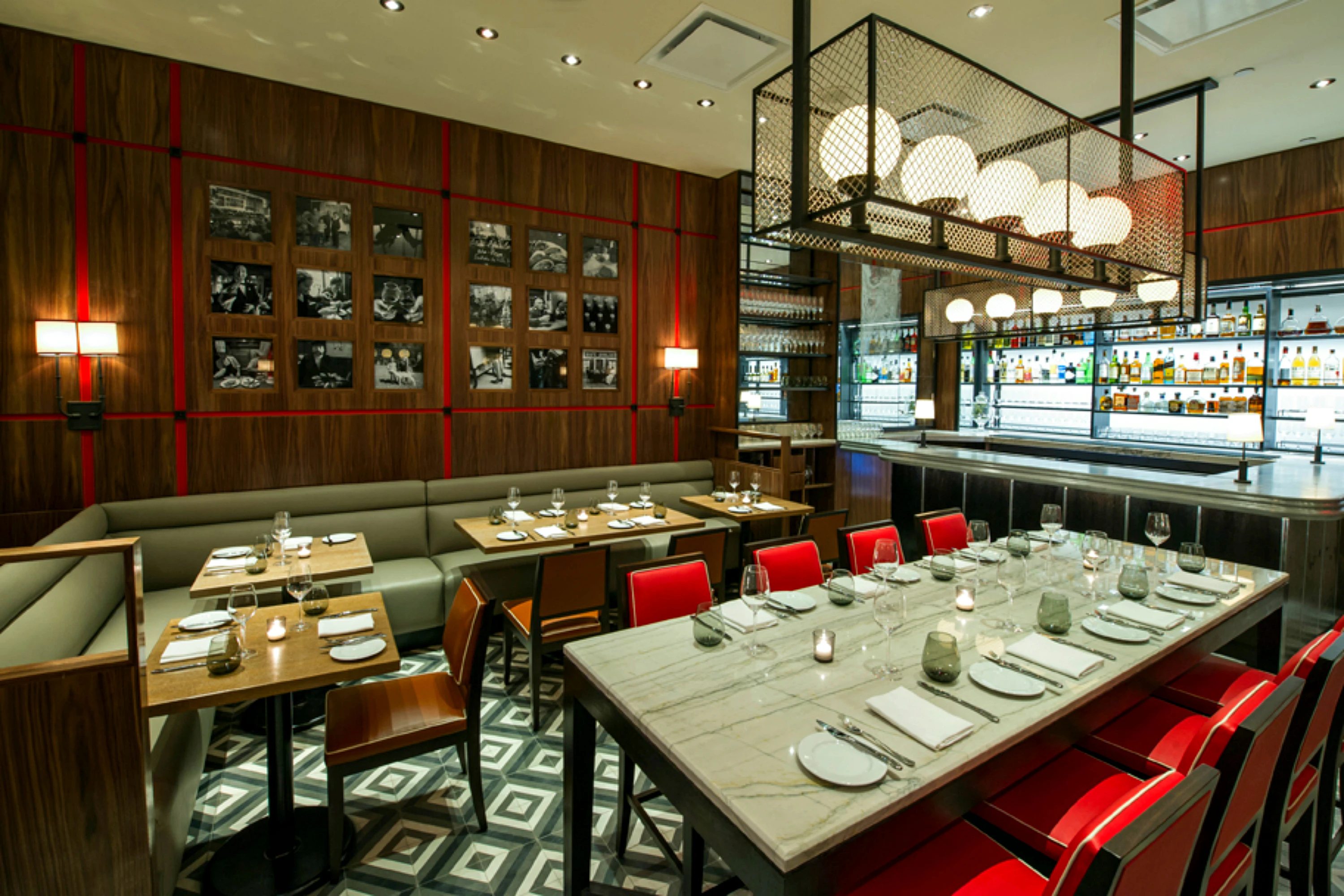 A dining area with a long marble table and red chairs, booth seating, and a chandelier.
