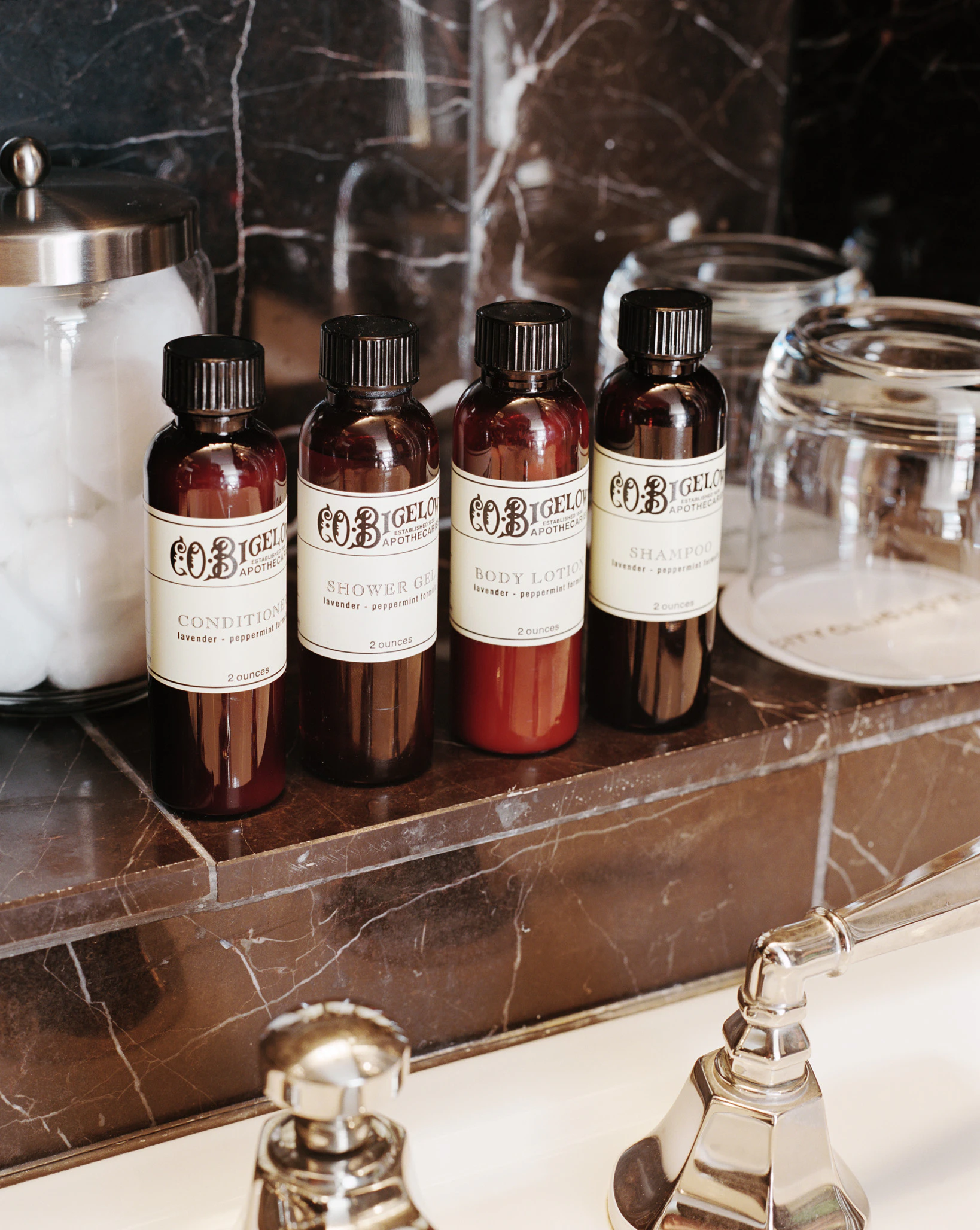 a bathroom counter with bottles of shampoo, conditioner, body lotion, and shower gel