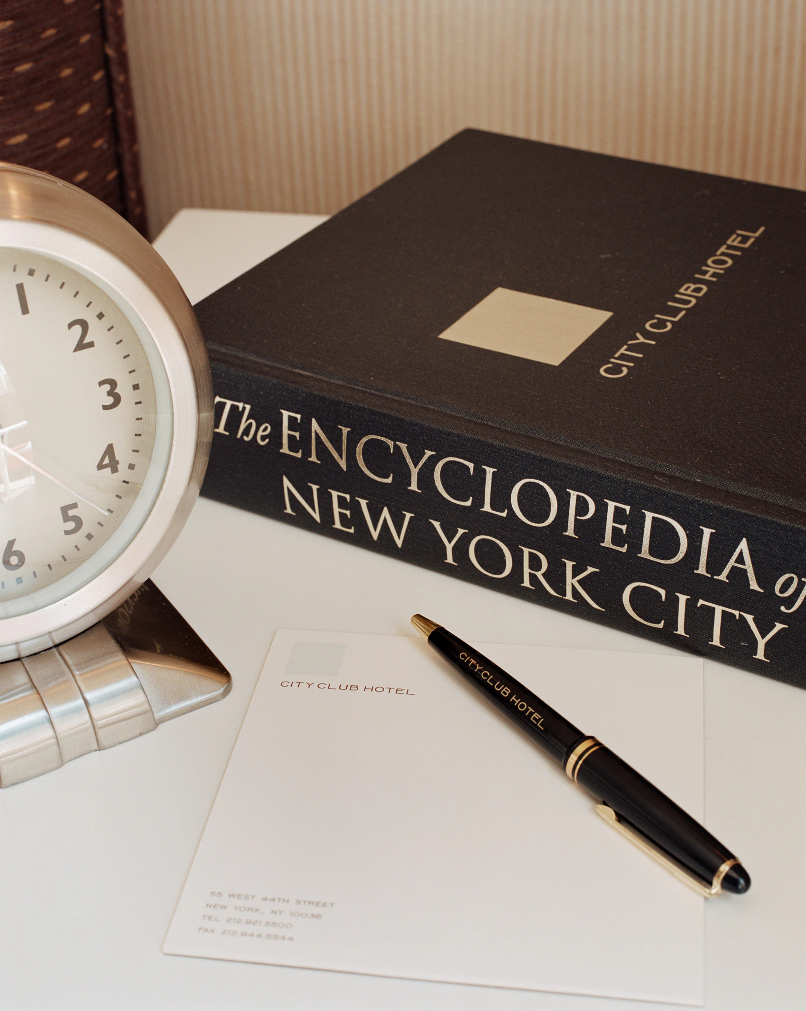 A hotel desk with a clock, pen, notepad, and book.