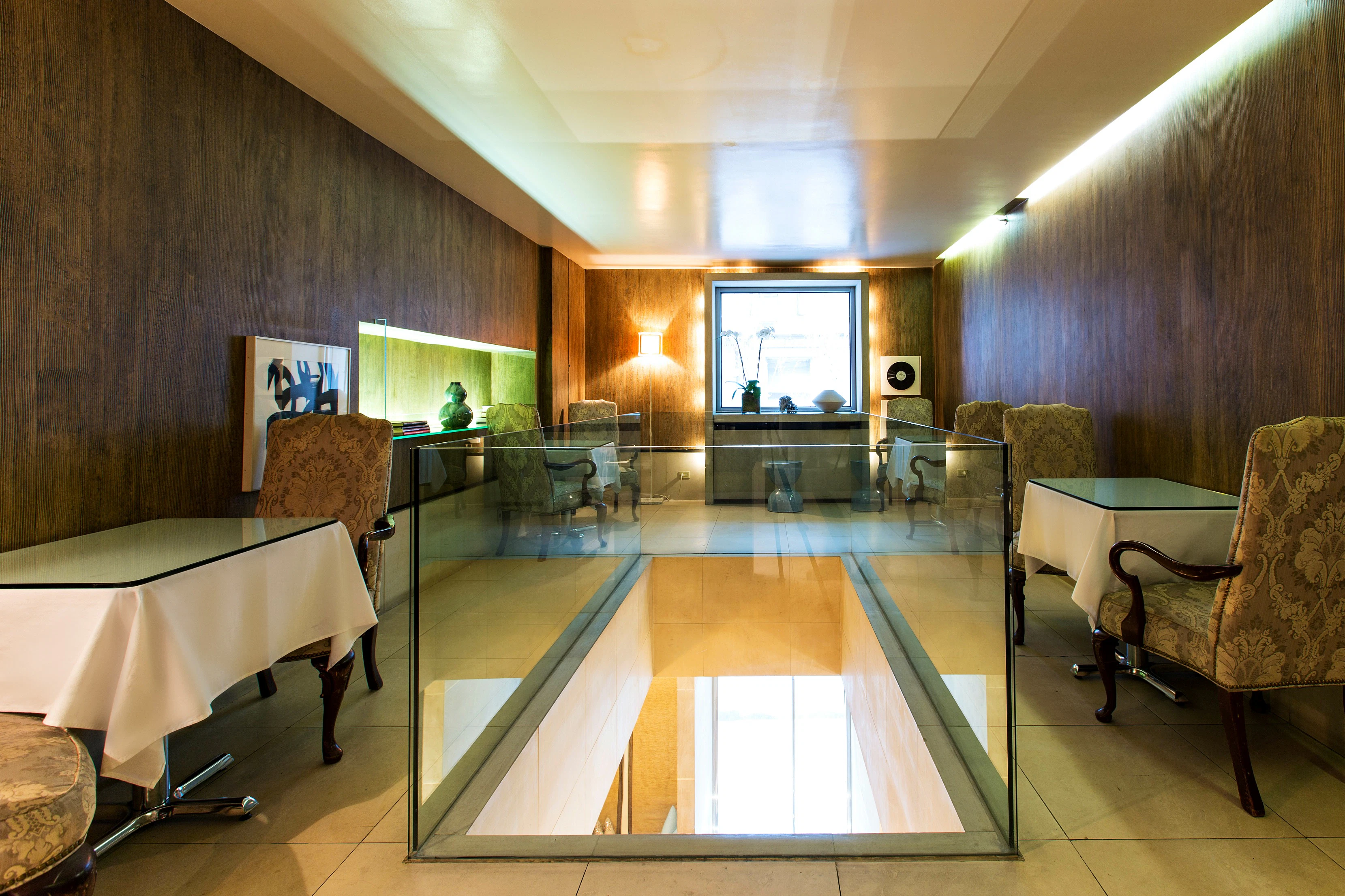 A lobby with a glass partition, chairs, tables, and artwork.