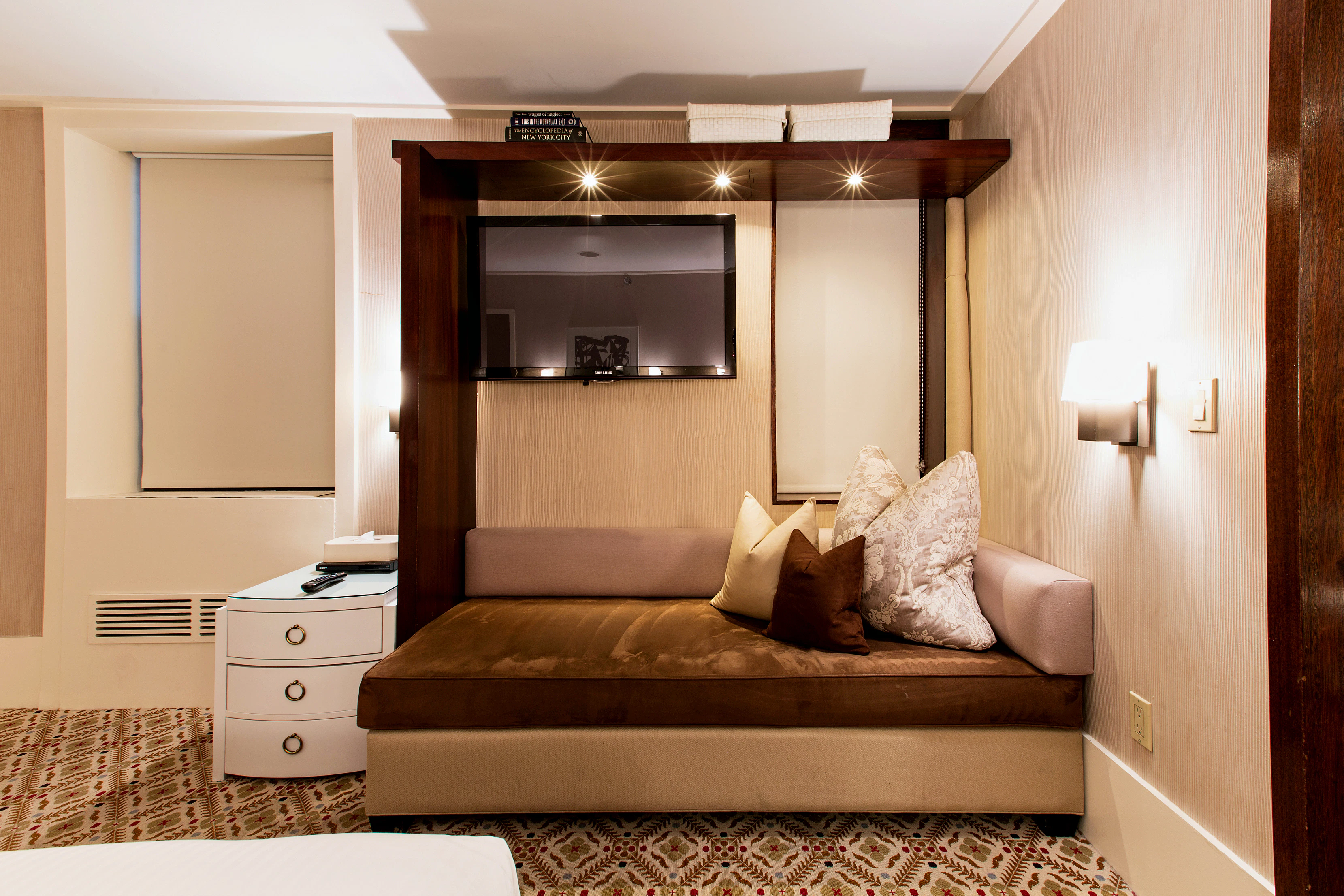 A luxurious hotel room with a brown sofa bed, white nightstand, and flat-screen TV.