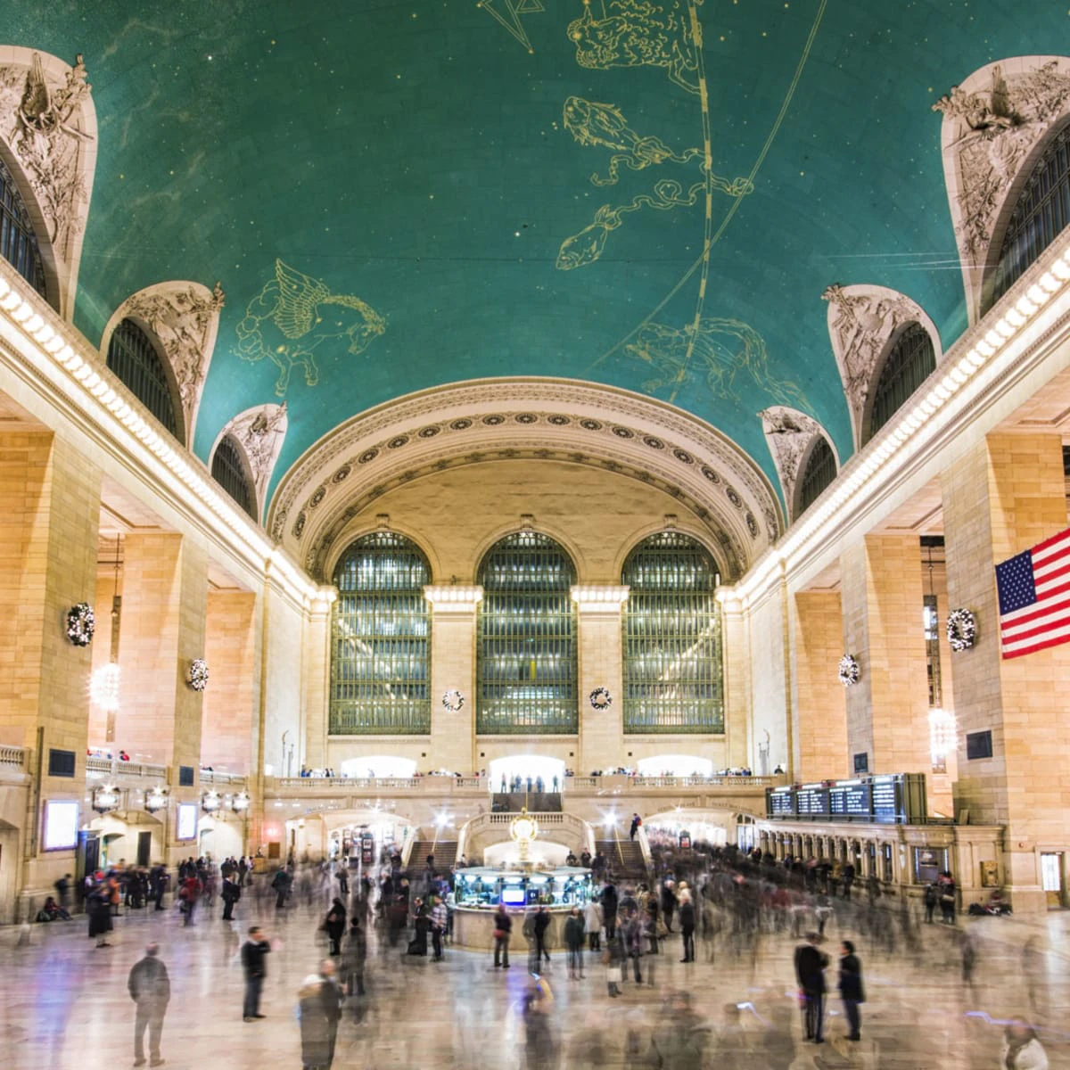 A large, ornate interior space with a high ceiling, arched windows, and a crowd of people.