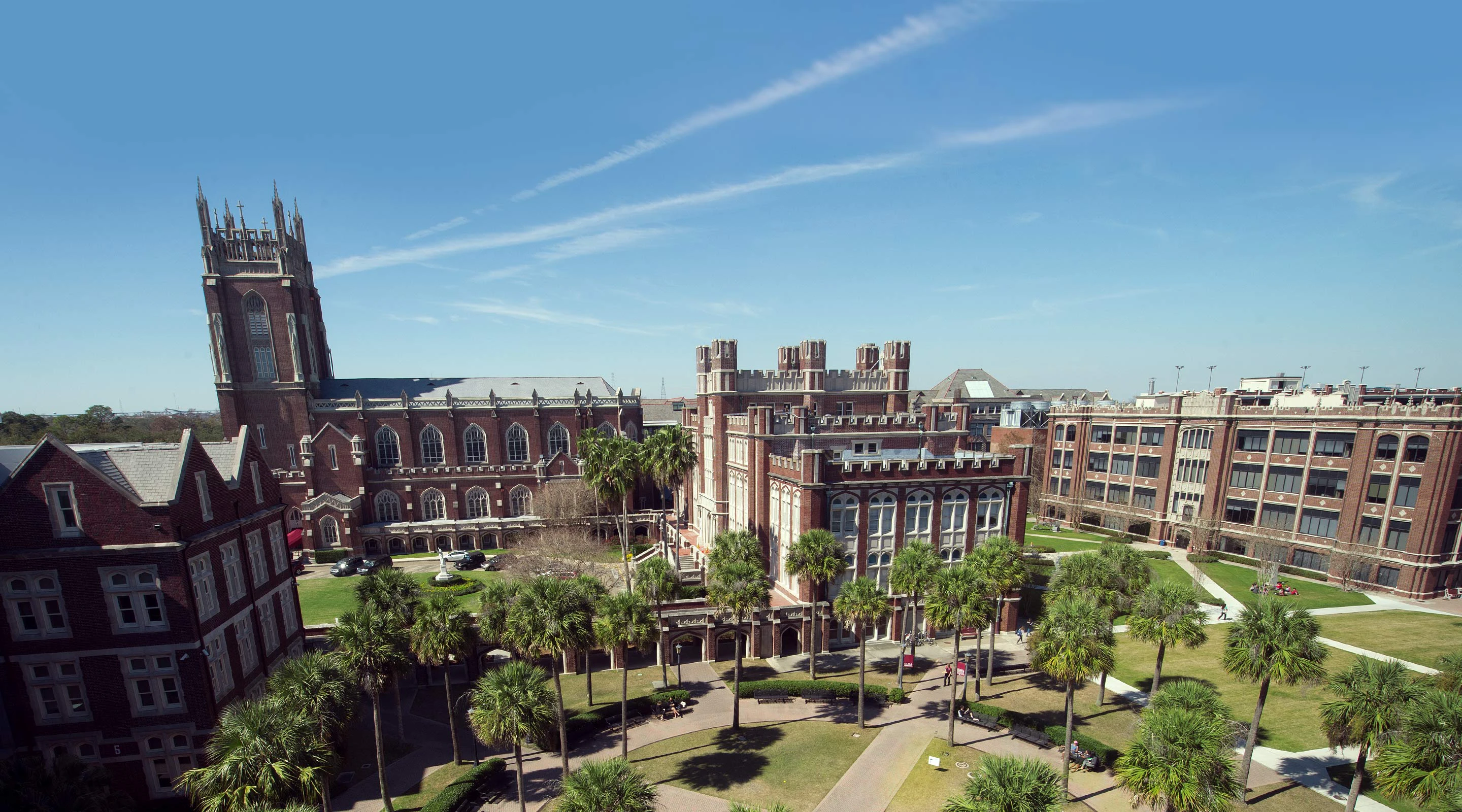 A large brick building with a tall tower and palm trees in a courtyard