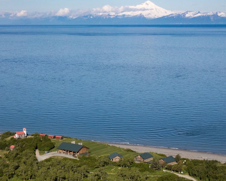 View of the lighthouse, the lodge and guest cabins set on a bluff with views of Cook Inlet, Mt Redoubt & Mt Iliamna.