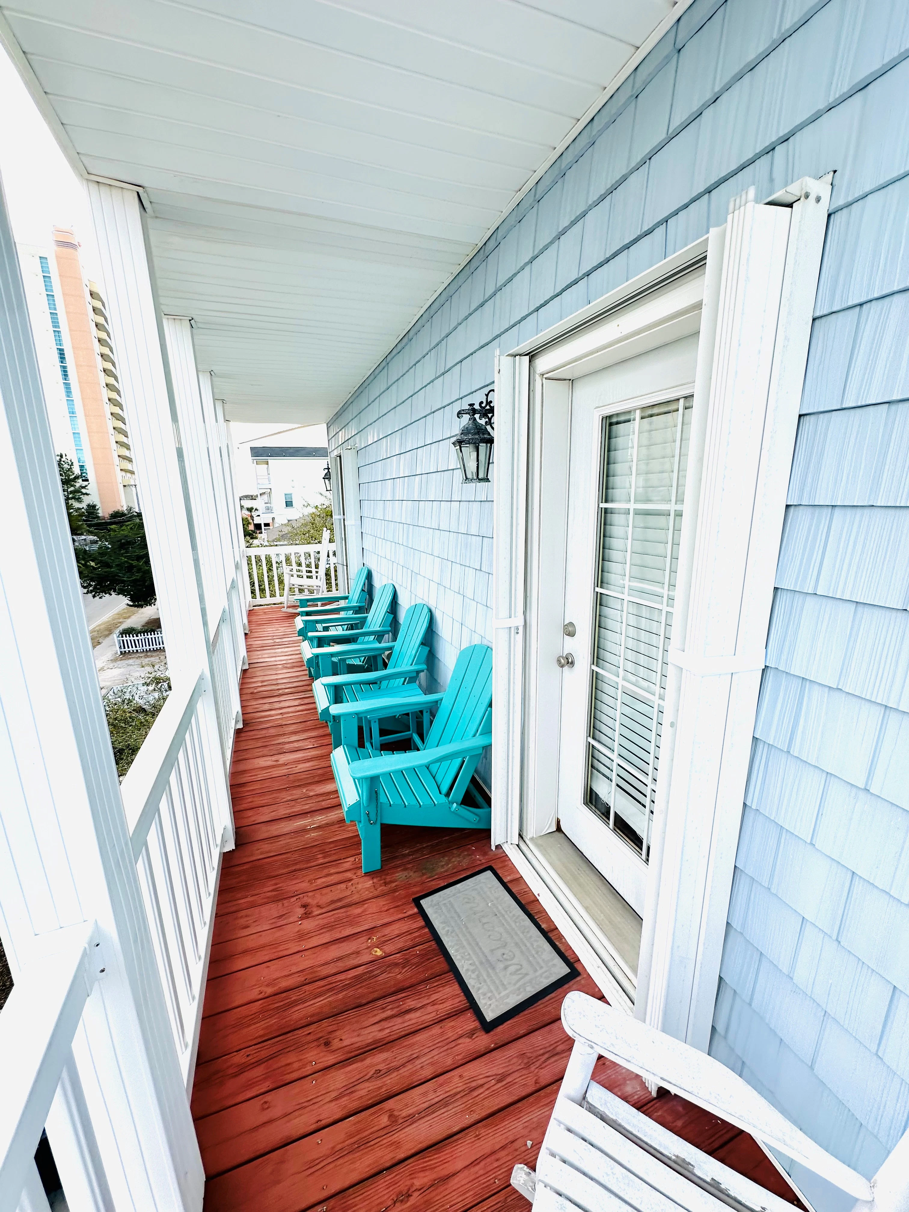 A porch with blue siding, red deck, and teal chairs