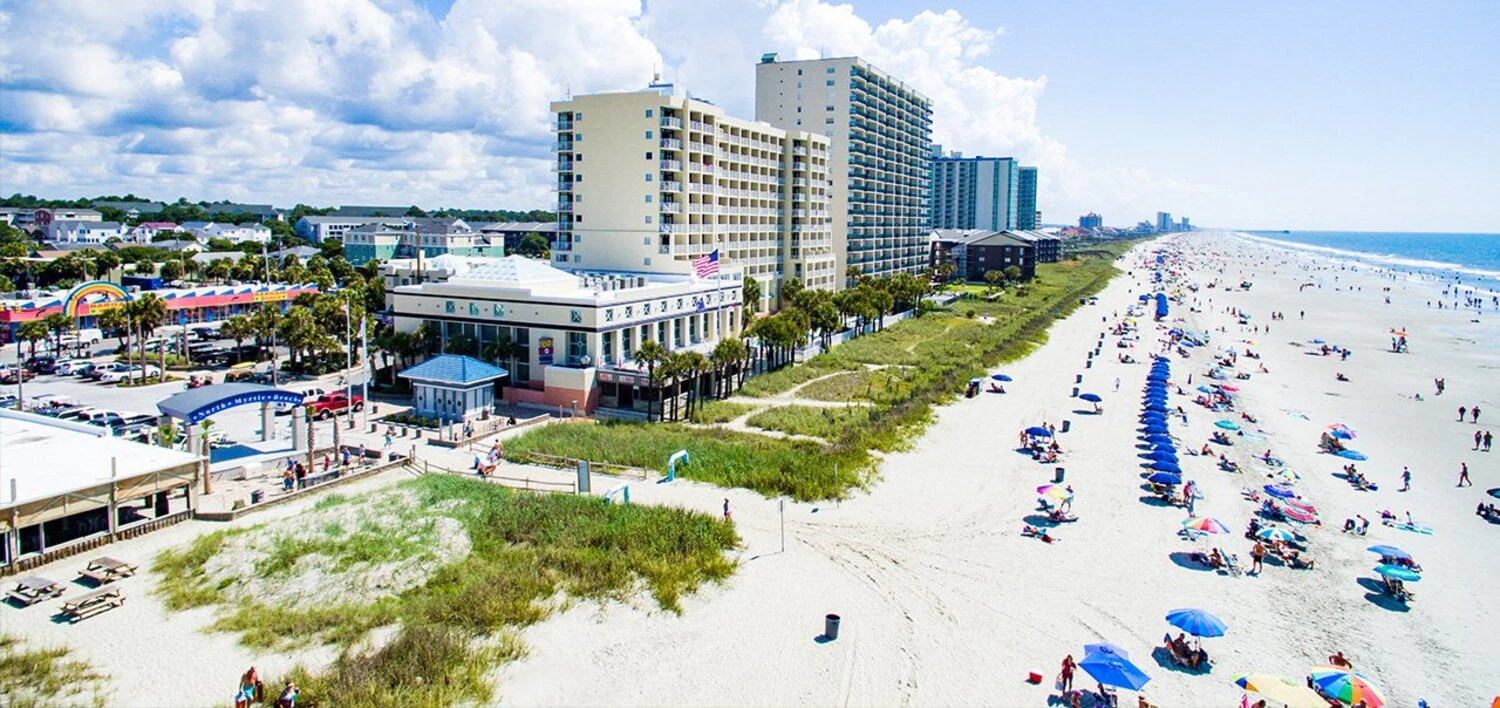 A wide-angle view of a beach with buildings and a blue sky with clouds.