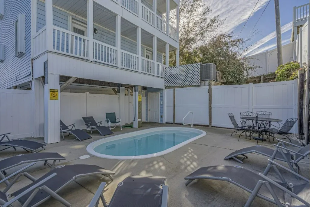 A pool area with lounge chairs and a table in front of a building.
