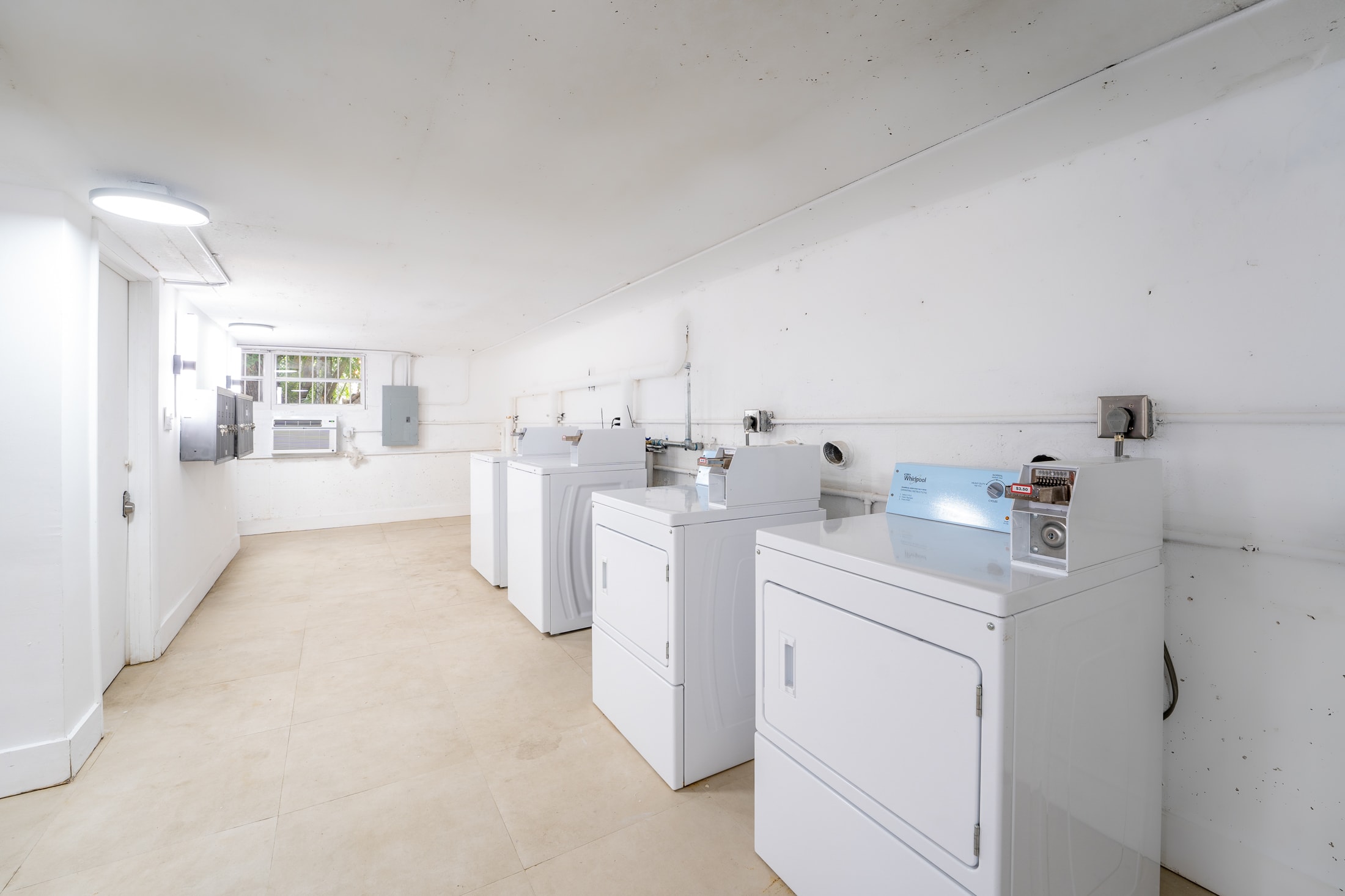 A row of white washers and dryers in a clean, well-lit laundry room with tiled floors and white walls.