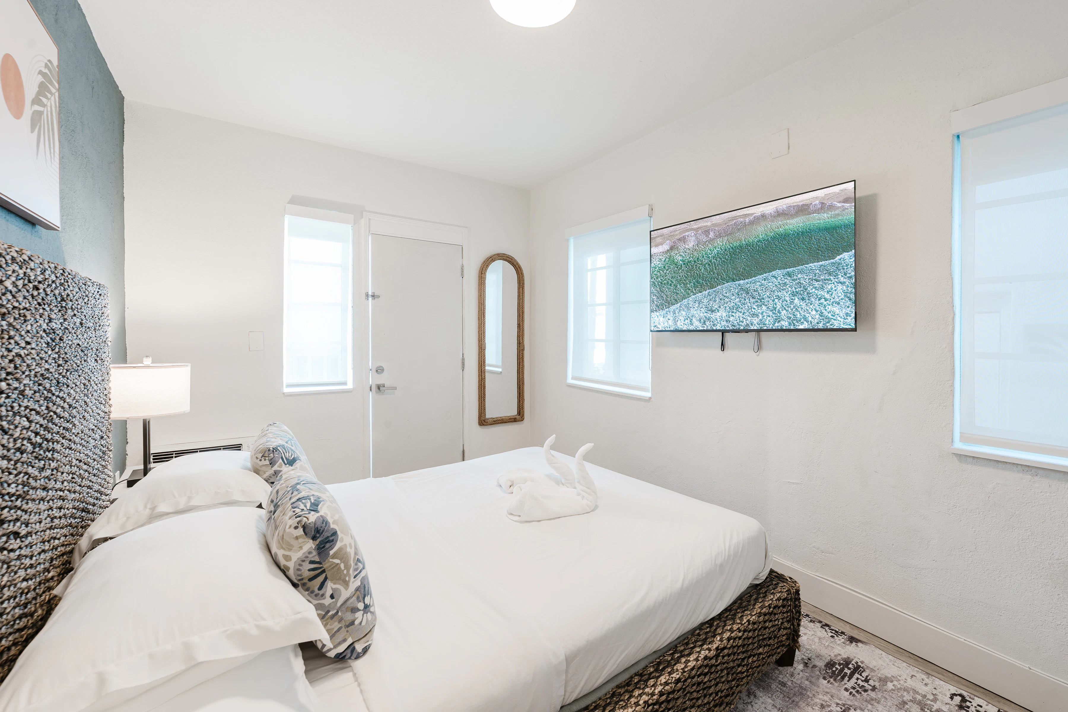A neatly arranged bedroom with a large bed, TV, lamp, and mirror.