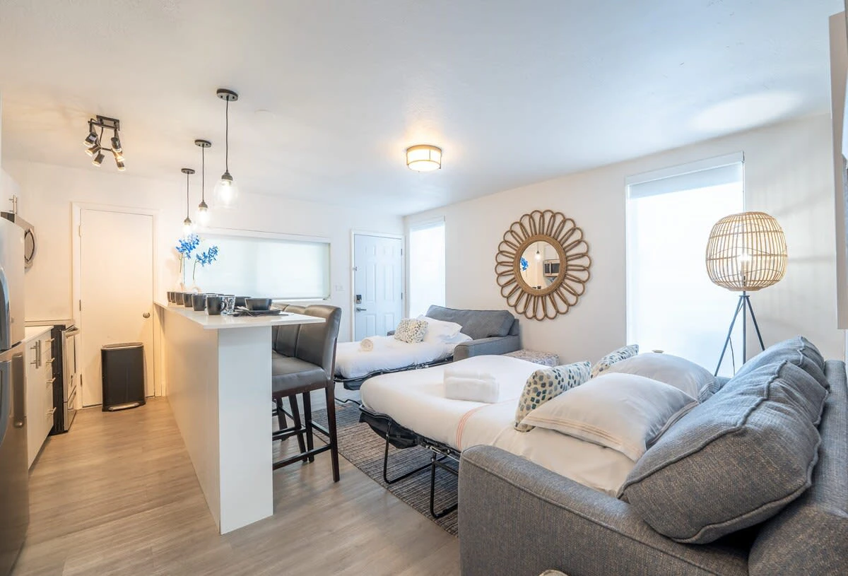 A bright and airy living room with a sofa bed, kitchenette, and dining area.