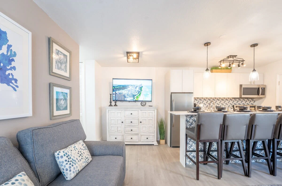 A wide view of a modern living area with a sofa, kitchenette, and TV.