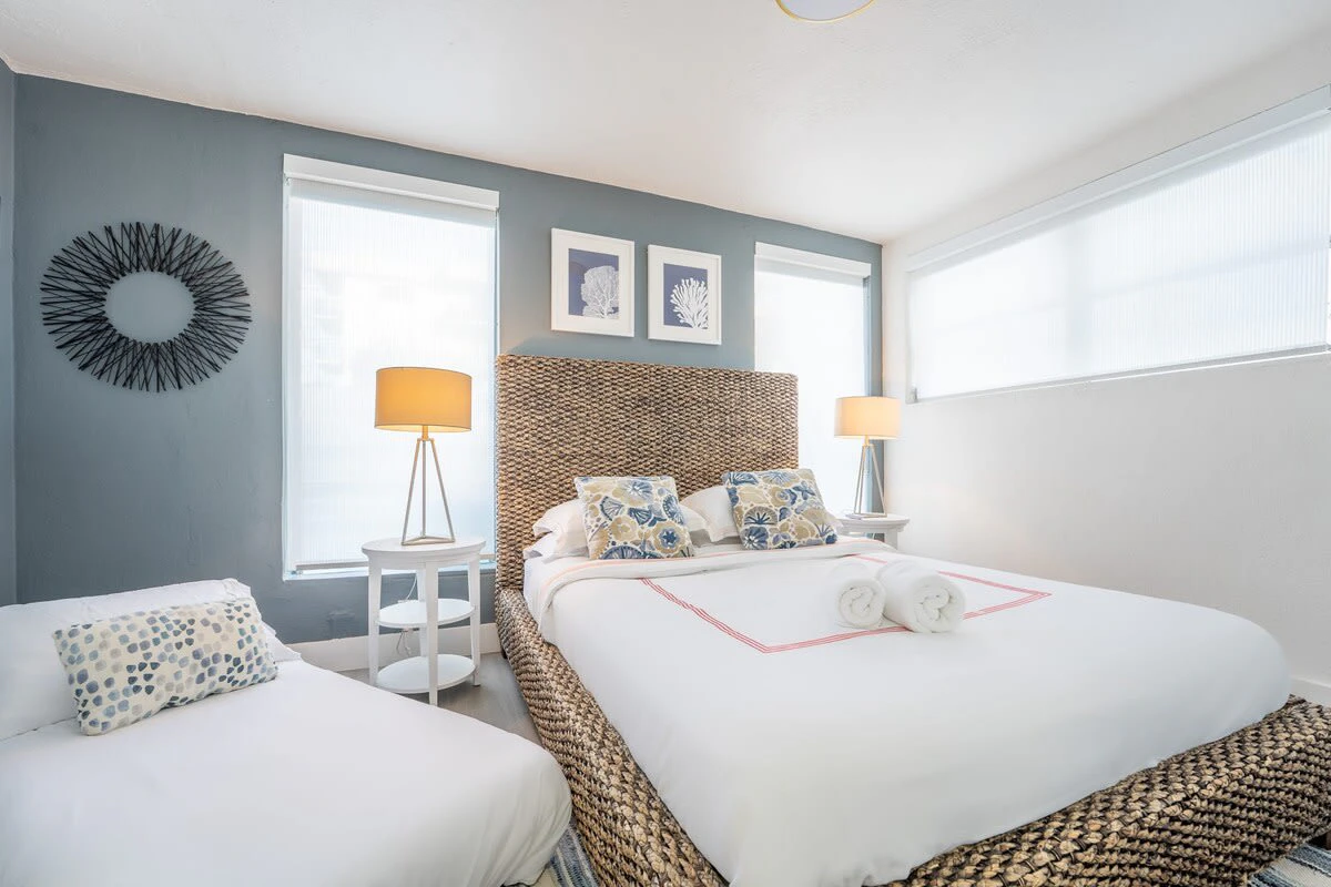A hotel room with two beds, a woven headboard, and blue walls.
